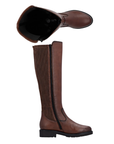 A pair of brown leather knee-high riding-style boots with stretch fabric over back of calf,  burnished accents and a deep treaded black outsole.