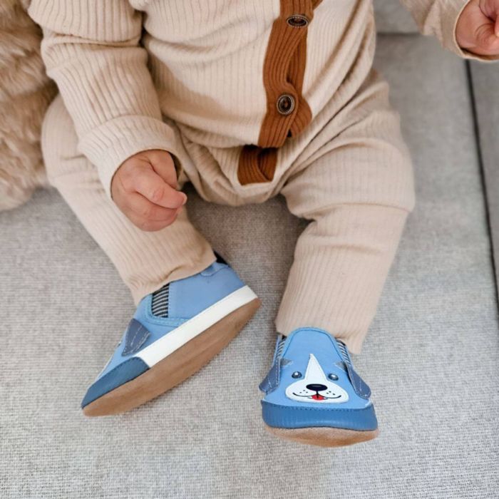Baby sitting with blue dog canvas shoes on.