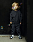 Toddler in black comfy clothes with bubbles floating around wearing the safari animal baby shoes