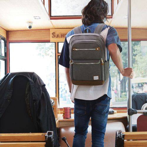 Man wearing gray Travelon Anti-Theft Heritage Backpack on public transport, showcasing its stylish design and travel-ready features.