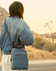 Person with a slate blue crossbody bag standing on a road in a desert landscape