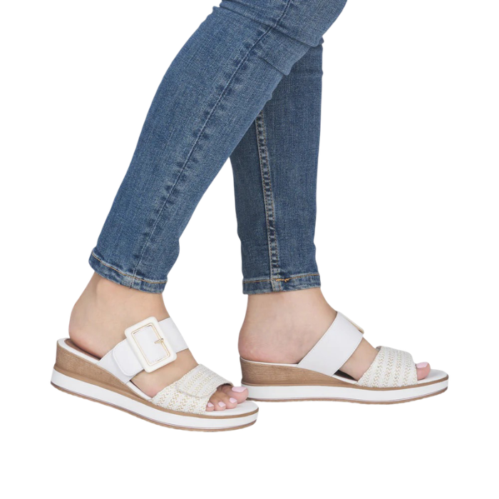 White slide wedge sandals with gold accents worn with blue jeans.