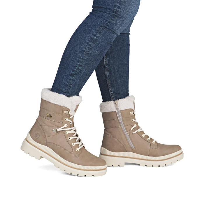 A pair of women's mid-calf lace-up boots in taupe with white faux-fur trim and a side zipper, shown on a model wearing blue jeans.