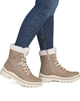 A pair of women's mid-calf lace-up boots in taupe with white faux-fur trim and a side zipper, shown on a model wearing blue jeans.