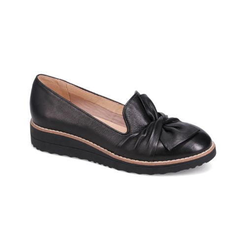 A black leather loafer with a scrunchy bow detail on the vamp and a low wedge heel.