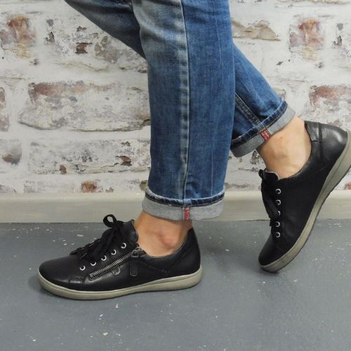 Model wearing jeans walking in the Caren 12 Sneakers in black. 