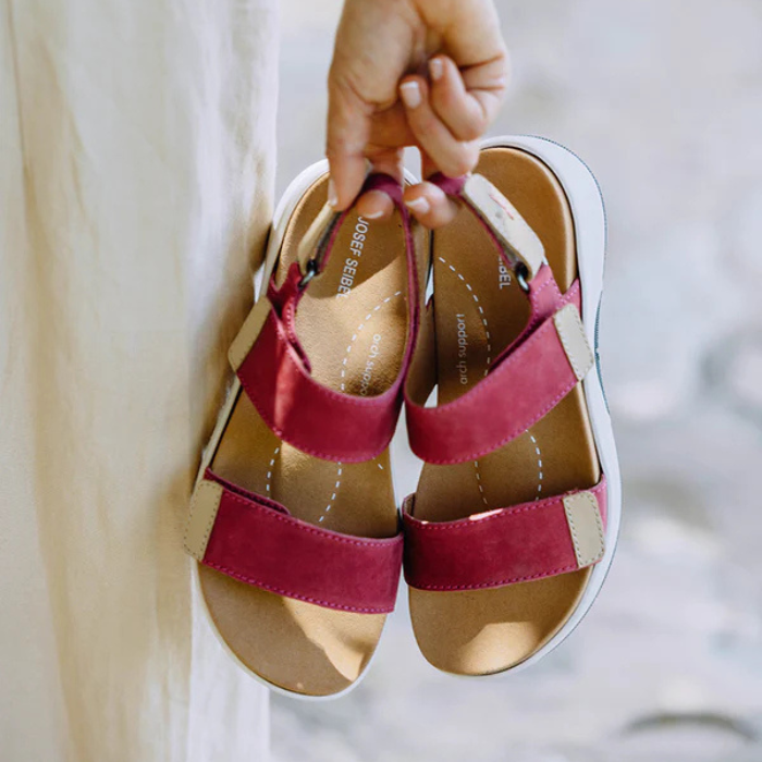 Women holding a pair of deep pink backstrap sandals next to beige pants.