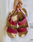 Women holding a pair of deep pink backstrap sandals next to beige pants.
