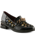 A glossy black leather loafer with dark yellow and blue floral pattern on the side panels, a decorative burnished gold metal rose on chain embellishment on the vamp, and black sculptured low block heel.