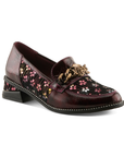 A glossy burgundy leather loafer with floral pattern on the side panels, a decorative burnished gold metal rose on chain embellishment on the vamp, and black sculptured low block heel.