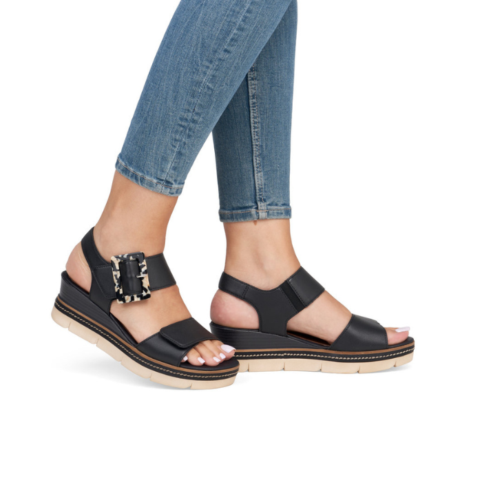 Black wedge sandals with decorative buckle worn with blue jeans.