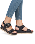Black wedge sandals with decorative buckle worn with blue jeans.