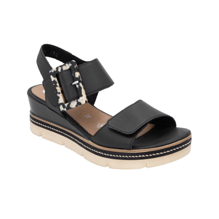 Black backstrap platform sandal with oversized decorative buckle, two Velcro straps, tan Remonte logo'd footbed, a faux wood grain wedge midsole and  an off-white outsole.