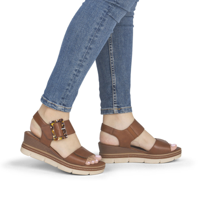 Brown wedge sandals with decorative square buckle worn with blue jeans.
