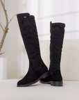 Black knee-high boots on a white surface with a minimal background