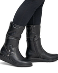 A pair of black leather mid-calf boots with side buckle straps worn with black  jeans.