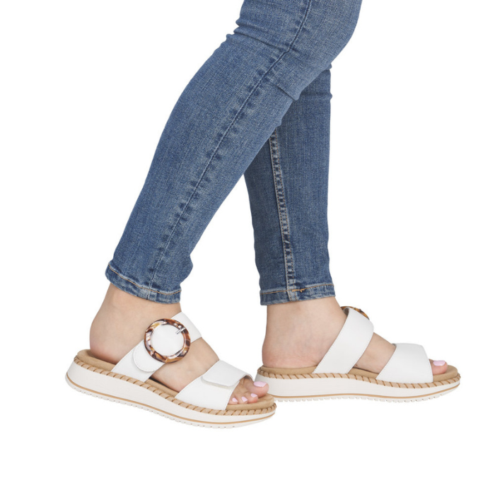 White sandals with a decorative buckle worn with blue jeans.