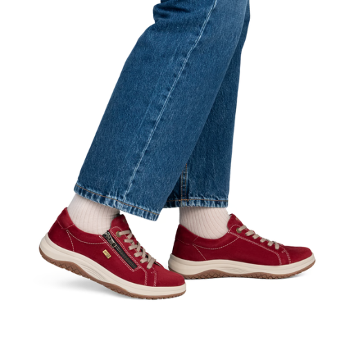 A person wearing red low-top sneakers with white socks and blue jeans, shown from the knees down.
