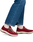 A person wearing red low-top sneakers with white socks and blue jeans, shown from the knees down.