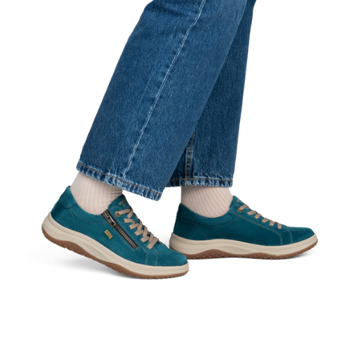 A person wearing blue jeans, white socks, and teal low-top sneakers with beige laces and a side zipper.