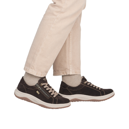 A person wearing beige pants and dark brown low-top sneakers with beige laces and outsole.