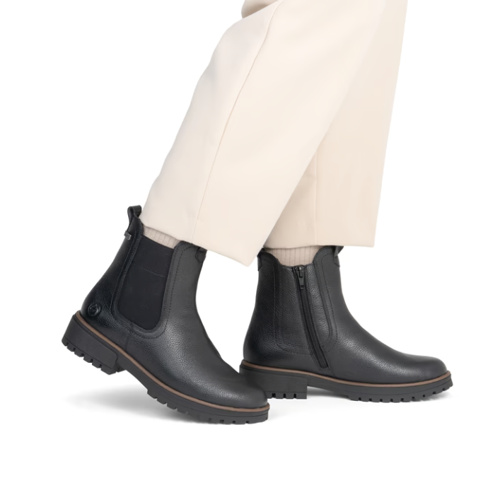 Black Chelsea boots worn with white dress pants.