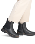 Black Chelsea boots worn with white dress pants.