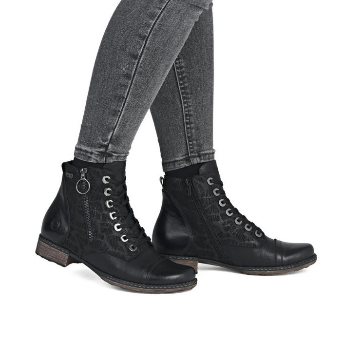 A pair of black lace-up ankle boots with side zippers and silver hardware, shown on a model wearing gray jeans.