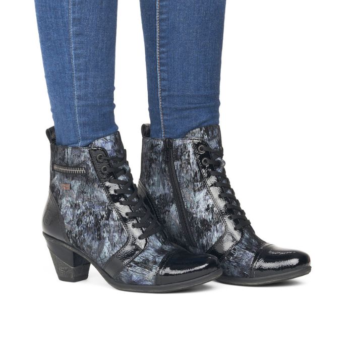 Legs in jeans wearing heeled ankle boot in blue and black with black patent toe cap.