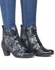 Legs in jeans wearing heeled ankle boot in blue and black with black patent toe cap.