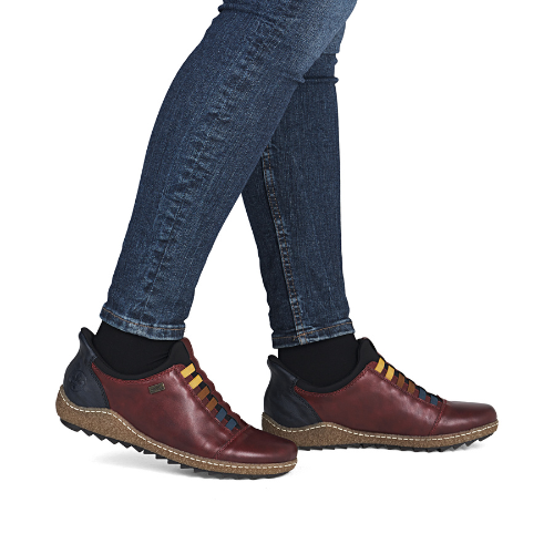 Red leather shoes with colorful elastic laces worn with blue jeans.