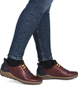Red leather shoes with colorful elastic laces worn with blue jeans.
