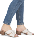 White sandals with bows and brown block heel worn with blue jeans.