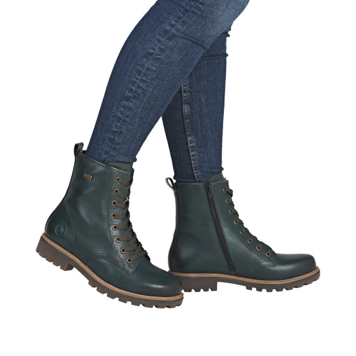 Green leather combat boots with brown soles worn with blue jeans.