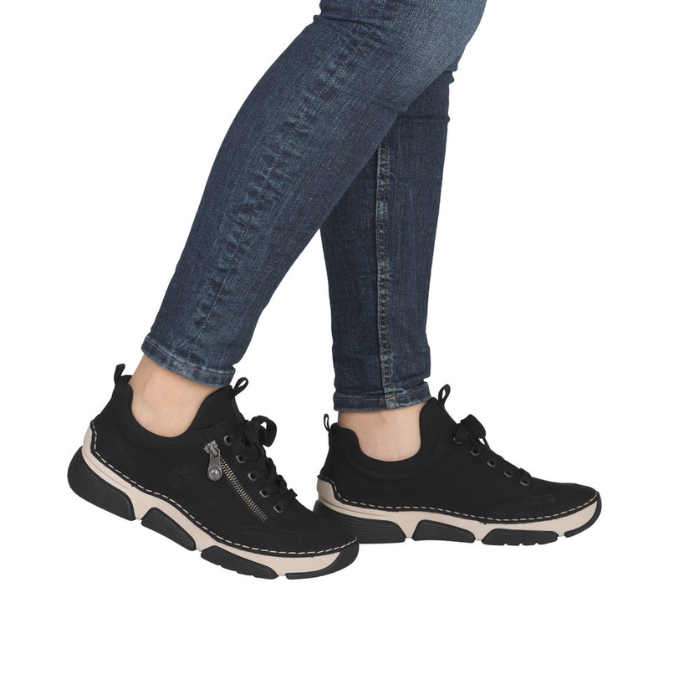 Black sneakers with beige midsole worn with blue jeans. 