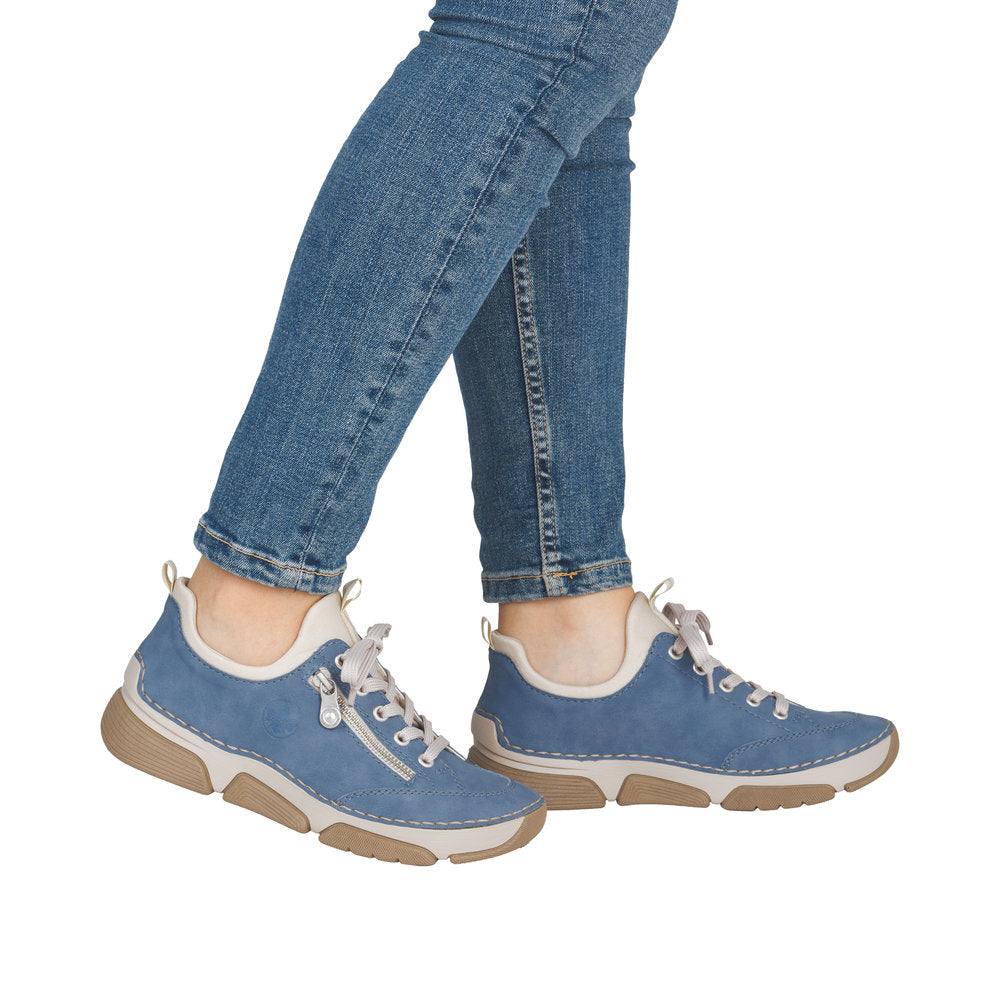 Blue sneakers with white midsoles and beige outsole accents worn with blue jeans.