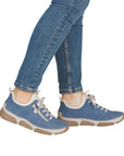 Blue sneakers with white midsoles and beige outsole accents worn with blue jeans.