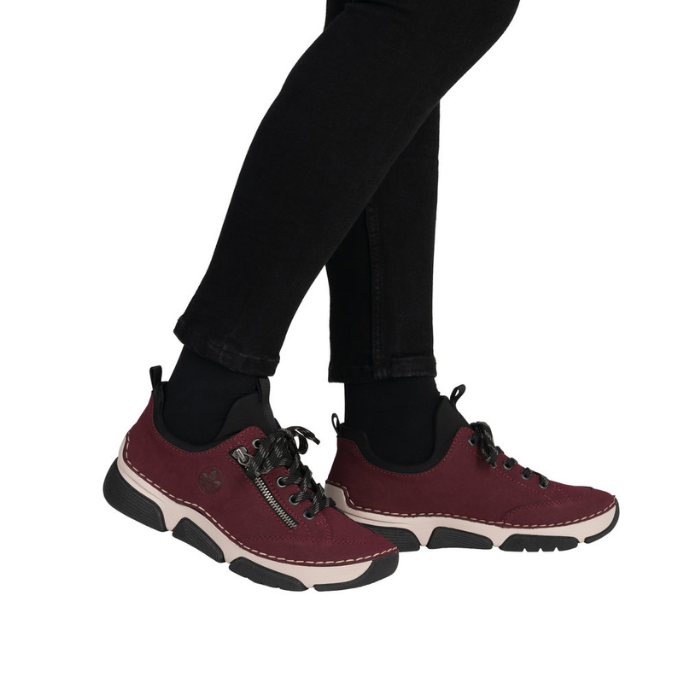 Deep red sneaker with  faux side zipper, accent stitching above the thick beige midsole and black outsole worn with black pants.