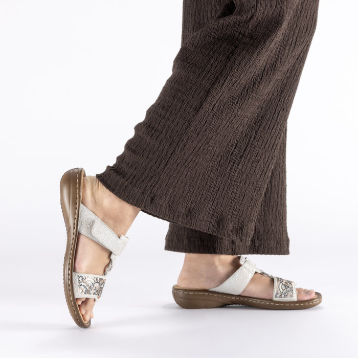 Woman wearing brown pants and silver slide sandals with decorative bead design.