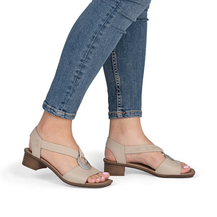 Beige low block heel sandals worn with rolled-up blue jeans.
