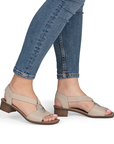 Beige low block heel sandals worn with rolled-up blue jeans.