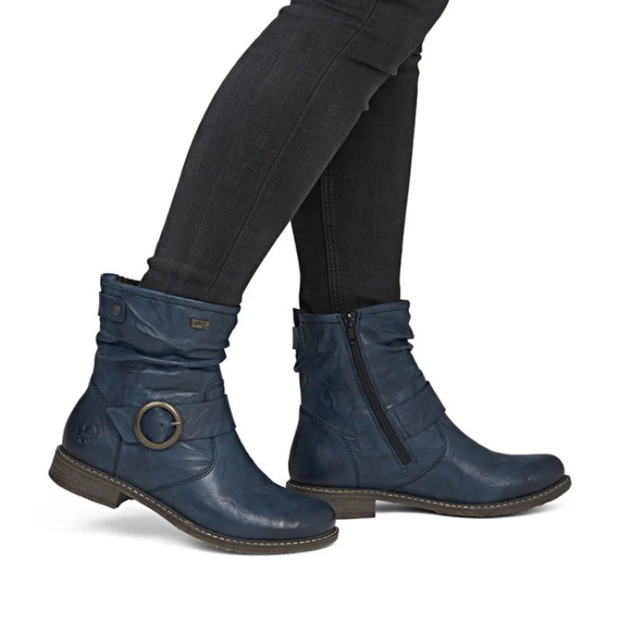 A pair of navy blue leather ankle boots with a buckle detail and side zipper, shown on a model wearing black skinny jeans.