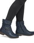 A pair of navy blue leather ankle boots with a buckle detail and side zipper, shown on a model wearing black skinny jeans.