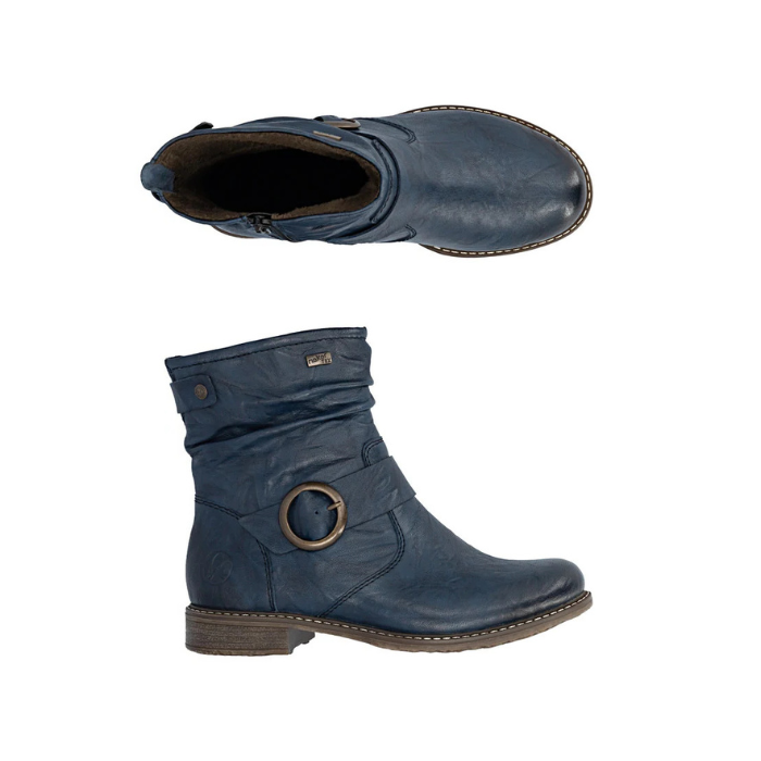 Pair of navy blue slouchy ankle boots with a brown sole, inside zipper and a bronze circular metal ring detail on the side.