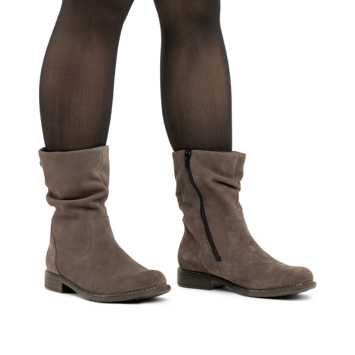 A pair of women's taupe-brown suede slouchy ankle boots with a side zipper, shown on a model wearing sheer black tights.
