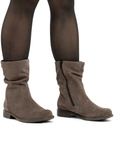 A pair of women's taupe-brown suede slouchy ankle boots with a side zipper, shown on a model wearing sheer black tights.