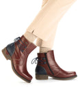 Legs in tan pants wearing red leather ankle boot with low heel, navy heel counter and navy lace detail on heel.