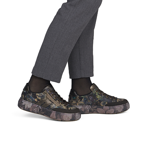 A person wearing dark gray trousers, black socks, and low-top sneakers with a dark floral camouflage pattern.