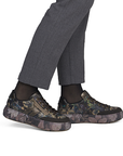 A person wearing dark gray trousers, black socks, and low-top sneakers with a dark floral camouflage pattern.