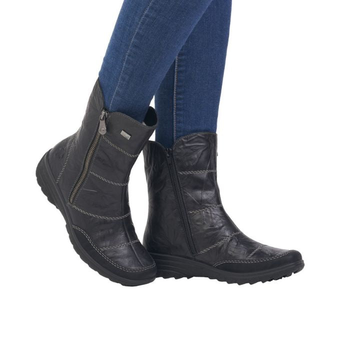 Legs in jeans wearing black leather mid-calf boot with beige accent stitching.